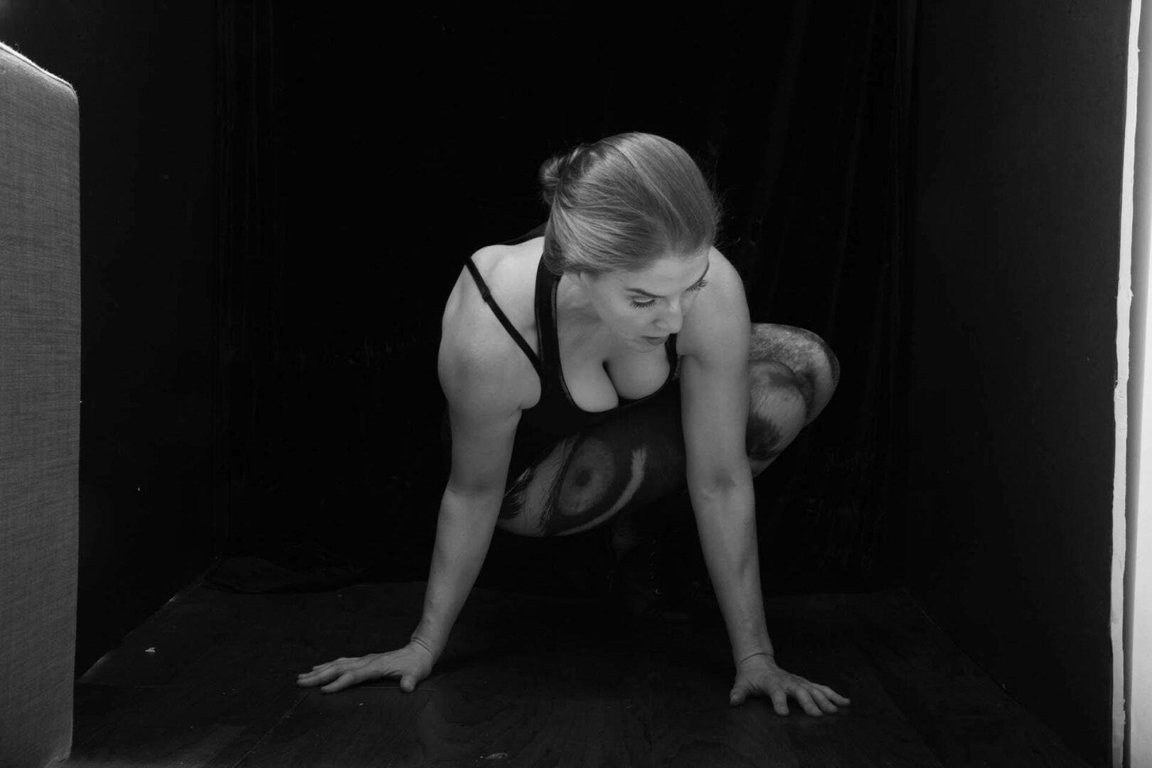 A woman in a black dress crouching on the floor against a dark background.